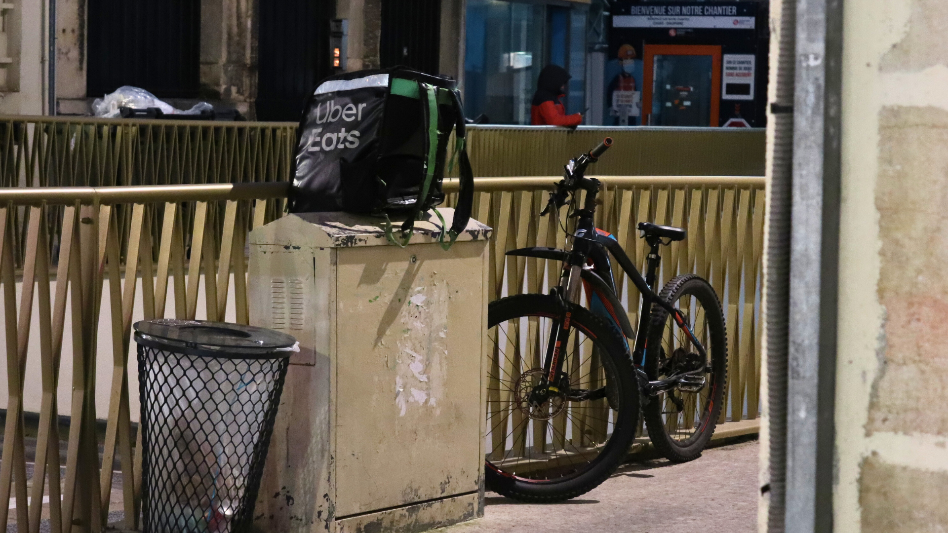 Un vélo de livreur posé contre une barrière et un sac Uber Etas en équilibre sur un compteur électrique.